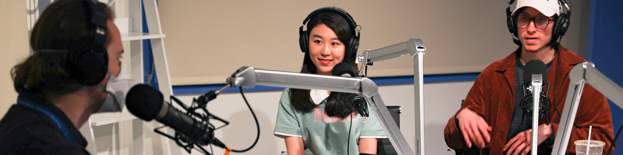 podcast in session with three people wearing headphones and sitting in front of microphones looking at eachother