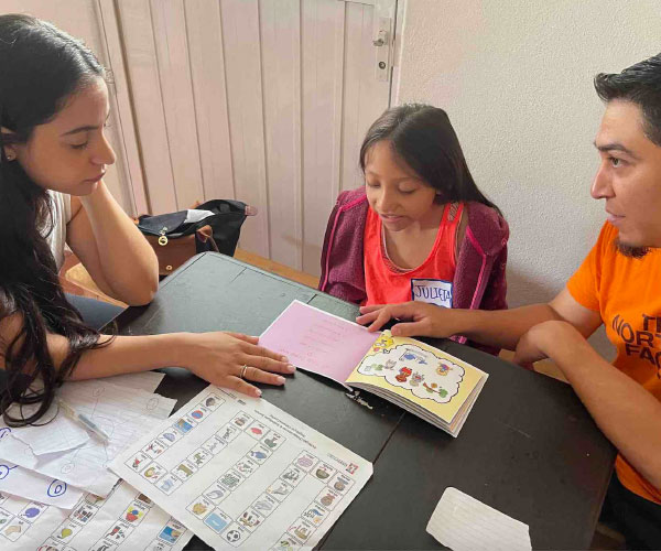 one child and two adults seated at a table in front of an open book with papers on the table