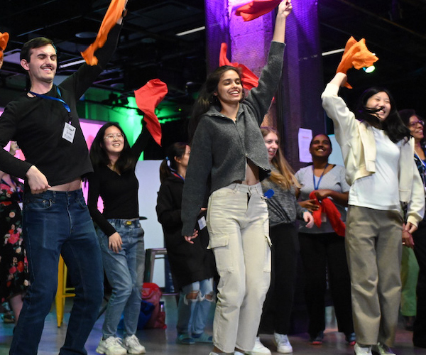 group of people in jumping motion with an arm raised holding colorful cloths in the air